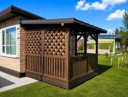 Attēlā redzama koka terase pie mājas ar saules paneļiem fona.